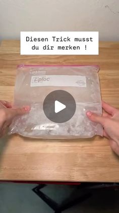 two hands holding an empty plastic bag on top of a wooden table next to a sign