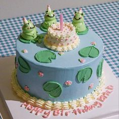 a birthday cake decorated with three little green frogs sitting on top of it's blue frosting