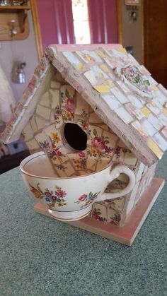 a tea cup and saucer sitting on top of a table next to a birdhouse