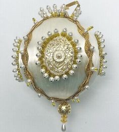 a white and gold ornament with pearls on the bottom, hanging from a chain