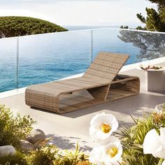 an outdoor chaise lounge on a balcony overlooking the ocean with flowers in blooming foreground