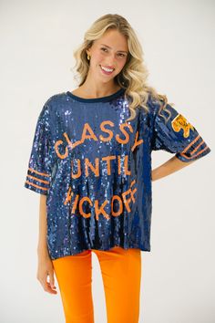 This CLASSY UNTIL KICKOFF TIGER SEQUIN TOP is the perfect way to show school spirit for the big game. Featuring a mix of navy and orange, this top let's you represent your team in style with a tiger patch accent on the sleeve. You'll be sure to stand out on gameday. All orders are currently shipping within 14 business days. To receive item quicker, expedited shipping is available at checkout. Varsity Tops For Cheerleading During Football Season, Collegiate Blue Tops For Cheerleading, School Spirit T-shirt For Cheerleading In Fall, Varsity Team-colored Tops For Game Day, Varsity Tops For Game Day, Varsity Style Tops For Football Season Game Day, Varsity Style Tops For Game Day, Varsity Tops With Team Name For Game Day, Cheerleading Fan Apparel Tops For Football Season