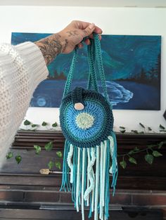 a hand holding a crocheted bag with tassels on it in front of a piano