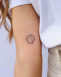 a woman's arm with a small shell tattoo on the left side of her right arm