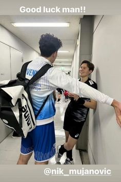 two young men are walking down the hallway with backpacks on their backs and one man is holding his hand out