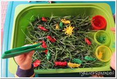 a child's hand holding a green plastic fork over a tray filled with fake grass