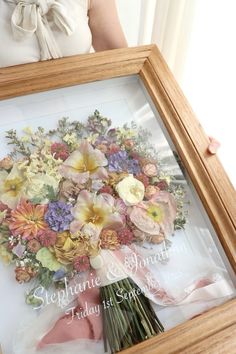 a woman holding a framed floral arrangement in her hands