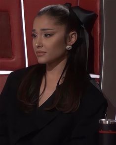 a woman sitting in a red chair with a black bow on her head and wearing earrings