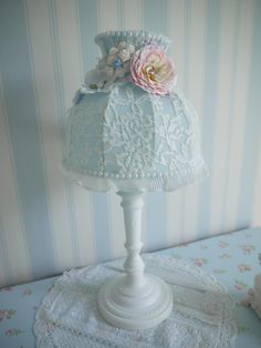 a white lamp with a pink flower on top of it next to a blue striped wall