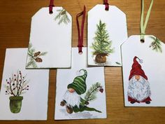 four tags with christmas gnomes and pine cones hanging from red ribbons on a wooden table