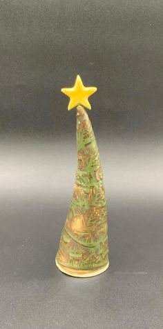 a small ceramic christmas tree with a yellow star on it's top, sitting on a gray surface