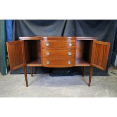 an old wooden cabinet with two doors and three drawers on one side, in front of a blue curtain