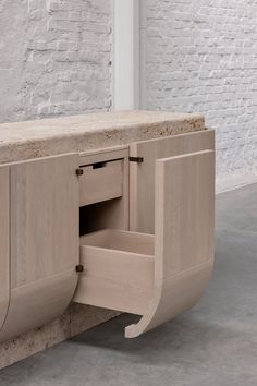 a wooden cabinet with an open drawer in front of a white brick wall and floor