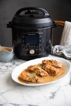 a white plate topped with meat and sauce next to an instant pressure cooker on a marble counter top