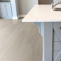 an empty kitchen with white counter tops and wood flooring