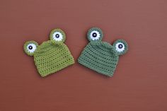 two crocheted hats with googly eyes are on a brown surface next to each other