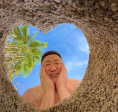 a man with his hands on his face looking through a hole in the sand that is shaped like a heart