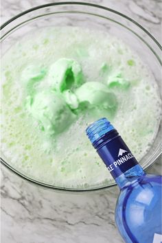 a glass bowl filled with green liquid next to a blue bottle