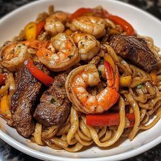 a white plate topped with pasta and meat covered in shrimp, bell peppers and carrots