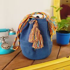 a blue purse sitting on top of a wooden table next to a phone and potted plant