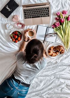 a woman sitting on top of a bed in front of a laptop computer next to food