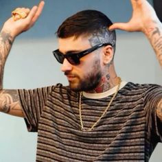 a man with tattoos holding his hands up in the air while wearing sunglasses and a striped t - shirt