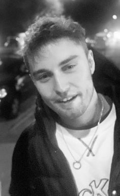 a black and white photo of a young man smiling at the camera with cars in the background