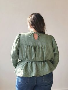 a woman standing in front of a wall with her back turned to the camera, wearing jeans and a green blouse