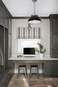 a desk with a computer on top of it in front of a window and cupboards