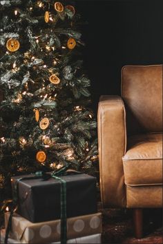 a christmas tree with presents under it in front of a chair and small gift box