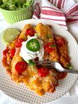 a white plate topped with enchiladas and a green bowl filled with salad