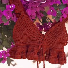 a crocheted bra hanging from a tree with purple flowers