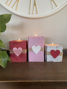 three wooden blocks with hearts on them sitting next to a plant and a wall clock