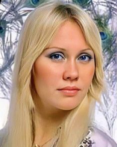 a woman with long blonde hair and blue eyes is posing for a photo in front of peacocks