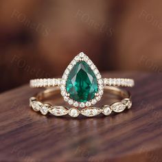 a pear shaped green diamond ring on top of a wooden table with diamonds around it