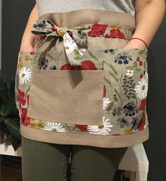 the woman is wearing an apron with flowers on it and has her hands in her pockets