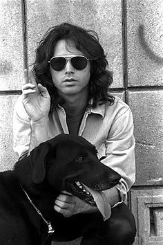 a man with sunglasses sitting next to a black dog on the ground in front of a brick wall