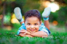 a little boy laying in the grass with his hands on his chest and smiling at the camera