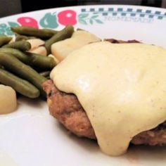 a white plate topped with meat covered in gravy next to green beans and potatoes