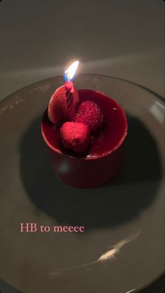 a small red bowl filled with raspberries on top of a white plate next to a lit candle