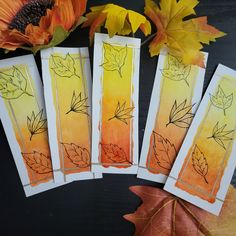 four cards with autumn leaves on them next to an orange and yellow flower arrangement in the background