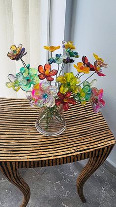 a glass vase filled with colorful flowers sitting on top of a wooden table next to a window