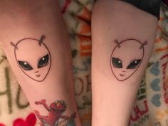 two people with matching tattoos on their legs, one has an alien face and the other has a red heart