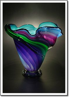 a colorful glass vase sitting on top of a black table next to a white wall