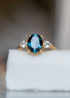 a blue and white diamond ring sitting on top of a white piece of cloth with diamonds around it