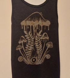 a black tank top with an image of mushrooms and leaves on the front, hanging on a wall