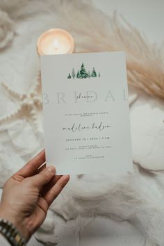 a person holding up a wedding card in front of a white background with some feathers