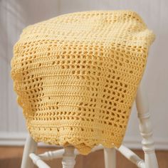 a yellow crocheted chair cushion sitting on top of a wooden floor next to a white chair