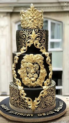 a three tiered black and gold wedding cake with a lion head on the top