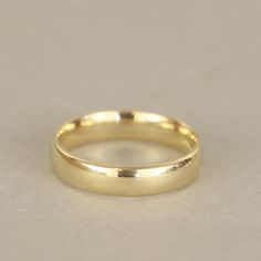 a plain gold wedding ring on a white surface with the top edge slightly down,